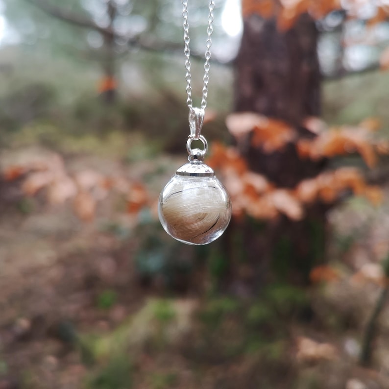 May include: A silver chain necklace with a clear glass orb pendant containing a lock of light brown hair.