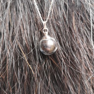May include: A silver chain necklace with a round, silver pendant. The pendant has a textured, metallic finish.