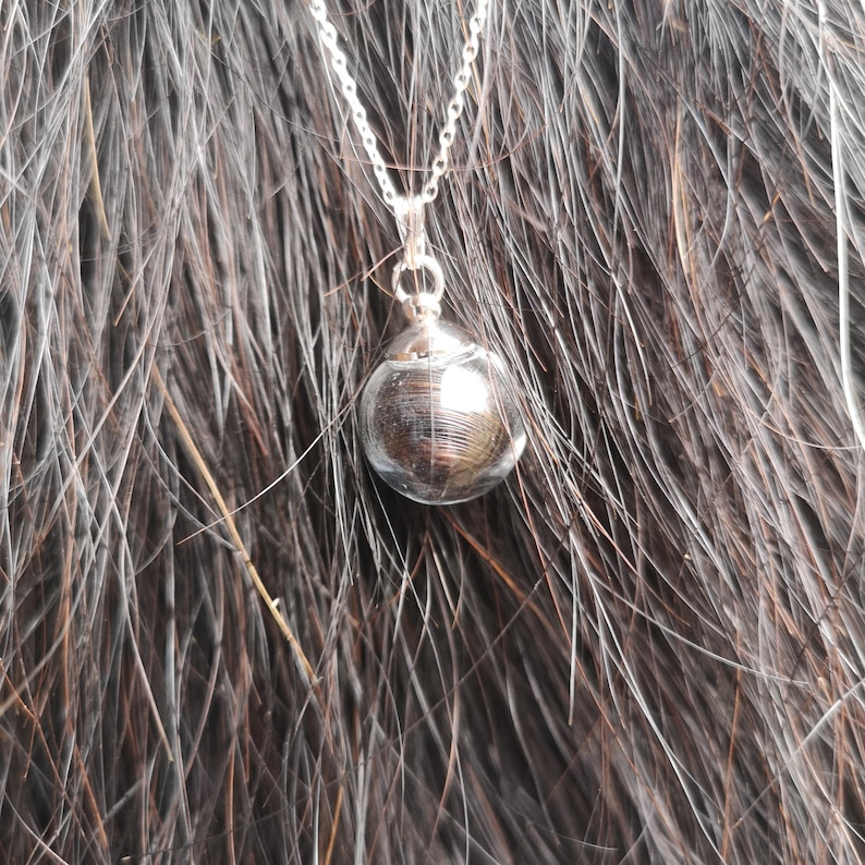 May include: A silver chain necklace with a round, silver pendant. The pendant has a textured, metallic finish.