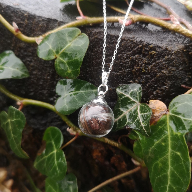 May include: A silver chain necklace with a clear glass orb pendant containing a swirl of brown hair.