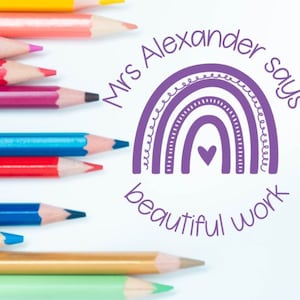 May include: A selection of coloured pencils alongside a purple rainbow design. The design features the text "Mrs Alexander says beautiful work". The pencils are in various colours, including yellow, pink, red, blue, and green.