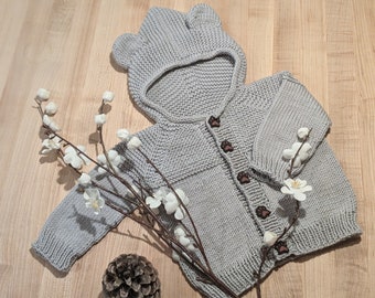May include: A gray knitted baby cardigan with a bear hood and brown paw print buttons.