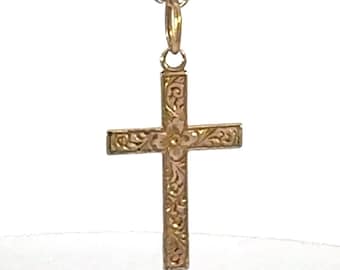 May include: A gold-coloured pendant necklace with a cross design. The cross features an ornate, engraved pattern and hangs from a delicate chain. The pendant is likely made of gold or a gold-toned metal.