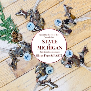 May include: Ornaments in the shape of the state of Michigan, made from a mosaic of stones. Each ornament has a small circular tag that says "Michigan". The text "STATE of MICHIGAN" is also visible.