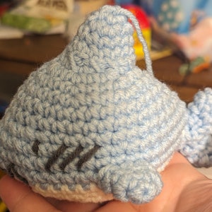 May include: A crocheted blue shark toy with a white belly and gray embroidered eyes.