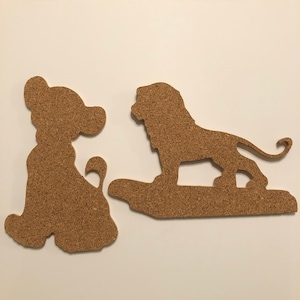 May include: Two corkboard silhouettes of a lion and a bear, both in a standing position. The lion is facing right and has a long tail. The bear is facing left and has a short tail. Both figures are cut out of corkboard and have a brown color.