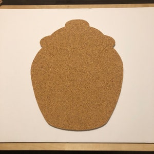 May include: A corkboard shaped like a jar with a lid. The corkboard is brown and has a rough texture.