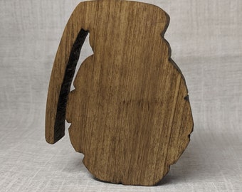 May include: A wooden cutout of a grenade, painted in a dark brown color. The cutout is detailed and has a rough texture.