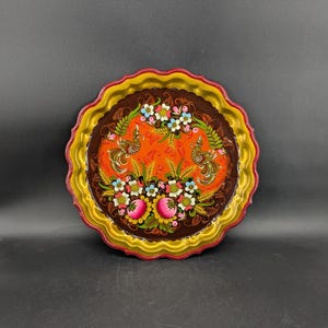May include: A round, wooden tray with a scalloped edge. The tray is painted with a colorful floral design featuring red, orange, yellow, green, blue, and white flowers. The tray is also decorated with two birds.