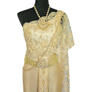 May include: A gold traditional Thai dress with intricate embroidery and a matching belt. The dress is on a black mannequin and has a sheer overlay.