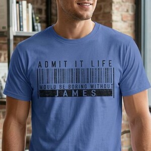 Puede incluir: Una camiseta azul de manga corta con un estampado gráfico negro de un código de barras. El texto dice ADMIT IT LIFE WOULD BE BORING WITHOUT JAMES. La camiseta tiene cuello redondo y un corte estándar, confeccionada en tela de color liso.