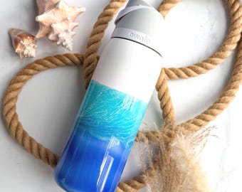 Könnte beinhalten: Eine weiß-blaue Trinkflasche mit Farbverlauf und dem Markennamen Owala auf dem grauen Deckel. Die Flasche zeigt ein Design, das von Weiß oben zu einem leuchtenden Türkis und tiefem Blau an der Basis übergeht und an Meereswellen erinnert.