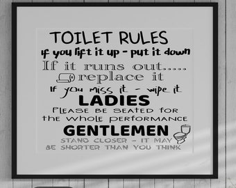 May include: A framed black and white print with bathroom rules. The text reads "TOILET RULES" followed by instructions. A white sink, vases, and decorative branches are in the foreground. The background is a white wood-paneled wall.