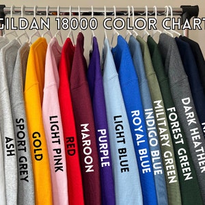 May include: Color chart for Gildan 18000 sweatshirts, showing 14 different colors: black, navy, dark heather, forest green, military green, indigo blue, royal blue, light blue, purple, maroon, red, light pink, gold, sport grey, ash, and white.