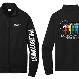 Puede incluir: Chaqueta de vellón negra con cierre de cremallera. La manga izquierda tiene el texto "PHLEBOTOMIST" impreso verticalmente en blanco. La manga derecha tiene el texto "MY JOB IS ALL RAINBOWS AND BUTTERFLIES" impreso en blanco. La parte posterior de la chaqueta tiene un gráfico de una jeringa y tubos de ensayo con líquido de color arcoíris.