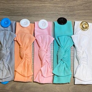 May include: Six headbands in different coloured fabrics with buttons. The headbands are tied in a bow and have a button on the top for holding a mask.