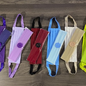 May include: Assortment of 10 fabric face masks with matching headbands. The masks are pleated and have a button on the side. The headbands are solid colours and come in blue, purple, lavender, red, light blue, beige, green, and yellow.