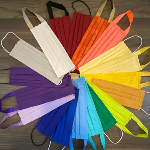 May include: A collection of 14 fabric face masks in a rainbow of colors, arranged in a circle. The masks are made of cotton and have adjustable ear loops.
