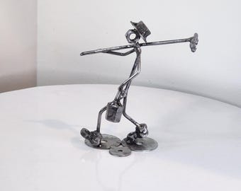 May include: A handcrafted metal sculpture of a person carrying a long pole with a bucket. The figure is made from metal rods, washers, and other metal pieces. The sculpture has a hat and is standing on metal washers.