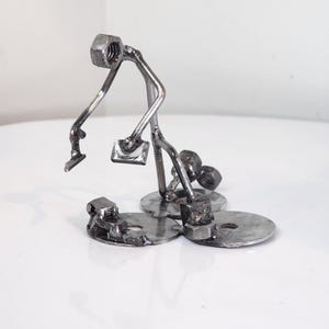 May include: A metal sculpture of a person holding a tool and standing on a base made of metal washers.
