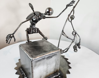 May include: A metal sculpture of a person doing a trick on a skateboard. The sculpture is made of recycled metal parts and is a unique piece of art.
