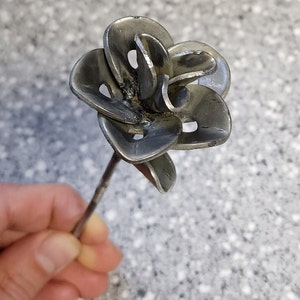 May include: A silver metal flower with multiple petals, crafted from recycled metal, is attached to a thin metal stem.