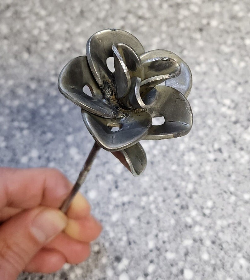 May include: A silver metal flower with multiple petals, crafted from recycled metal, is attached to a thin metal stem.
