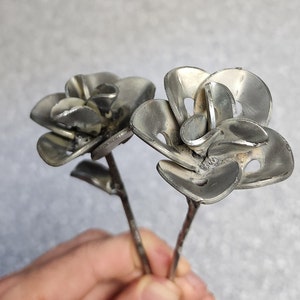 May include: Two silver metal roses with a stem and leaves. The roses are made from recycled metal and have a rustic, industrial look.