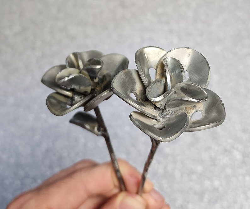 May include: Two silver metal roses with a stem and leaves. The roses are made from recycled metal and have a rustic, industrial look.