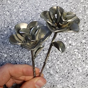 May include: Two metal flowers made from recycled metal parts. The flowers are silver in color and have a rustic look. The stems are made from thin metal rods.