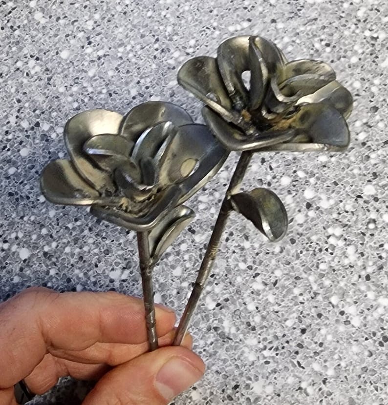 May include: Two metal flowers made from recycled metal parts. The flowers are silver in color and have a rustic look. The stems are made from thin metal rods.