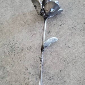 May include: A metal rose sculpture made from recycled metal parts. The rose is silver in color and has a single leaf. The sculpture is on a gray background.