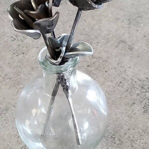 May include: Three metal roses in a clear glass vase. The roses are made of recycled metal and have a rustic, industrial look.