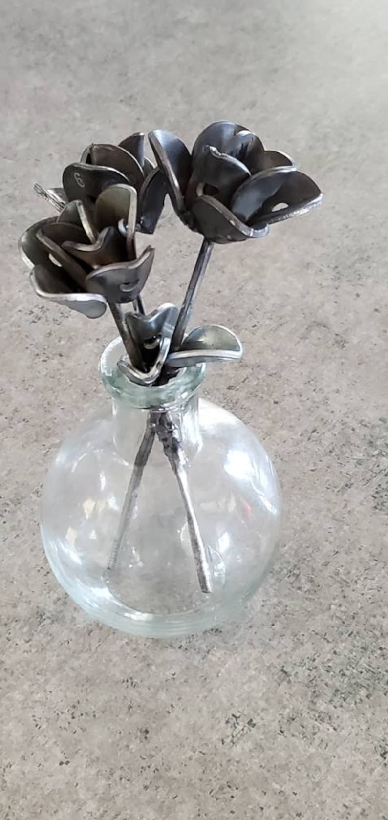 May include: Three metal roses in a clear glass vase. The roses are made of recycled metal and have a rustic, industrial look.