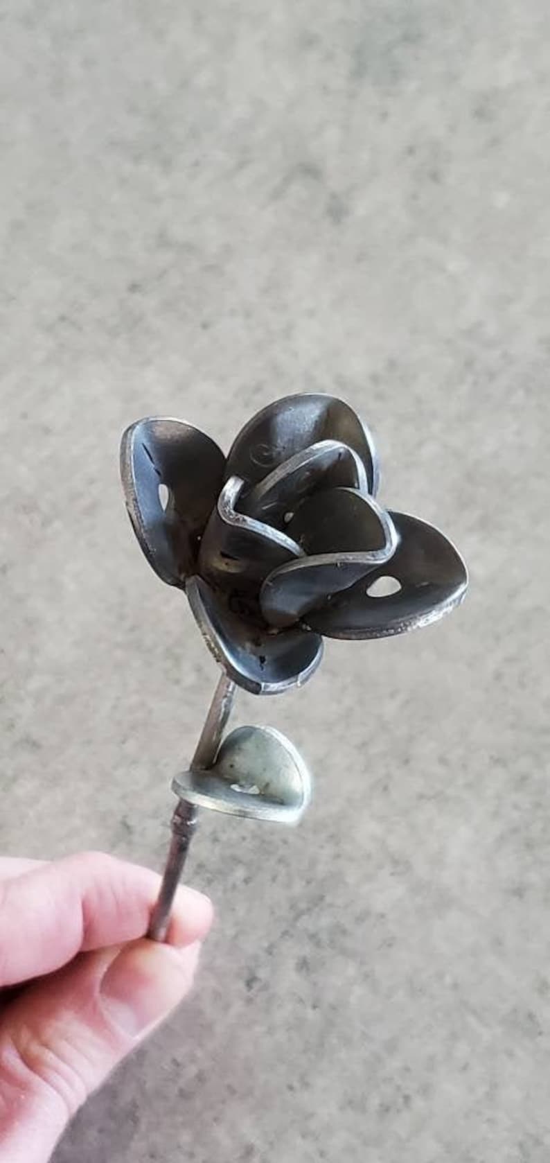 May include: A metal sculpture of a rose, made from recycled metal. The rose is silver in color and has a stem.
