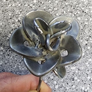 May include: A silver metal rose sculpture made from welded metal pieces. The rose is a unique and modern take on a classic flower.