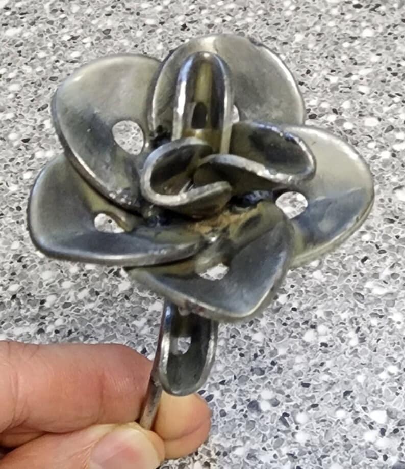 May include: A metal flower sculpture made from recycled metal washers. The flower has a stem and multiple petals with holes in them.