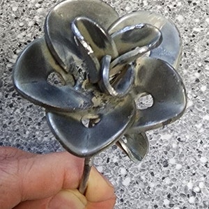 May include: A metal sculpture of a flower with multiple petals, crafted from recycled metal. The flower is silver in color and has a long stem.