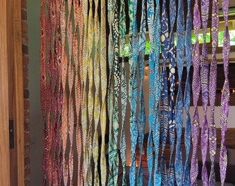 May include: Rainbow colored fabric curtain made of twisted strips of fabric. The curtain is hanging in a doorway.