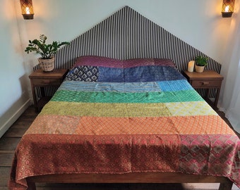 May include: A bed with a rainbow patchwork quilt and a black and white striped headboard. The bed is made of wood and has a wooden frame.