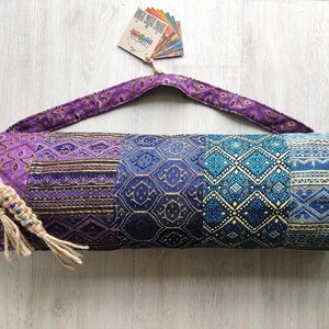 May include: Purple and blue yoga mat bag with a patterned design. The bag has a long strap and a drawstring closure.