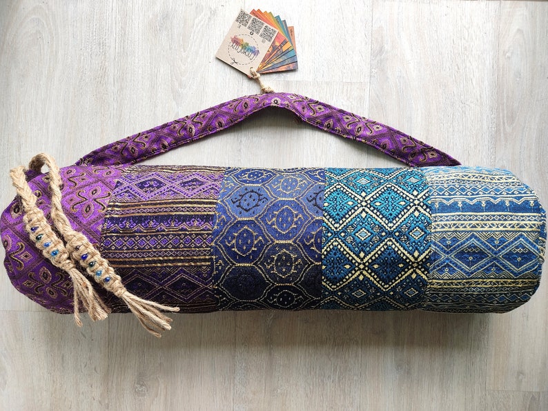 May include: Purple and blue yoga mat bag with a patterned design. The bag has a long strap and a drawstring closure.