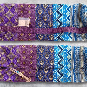 May include: Two purple and blue patterned yoga bolsters with a gold trim. The top bolster has a tag that reads "Cosmic Cozy".