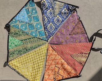 May include: A set of seven colorful fabric pennants with geometric patterns and gold accents. The pennants are arranged in a circle and are connected by black ribbon.