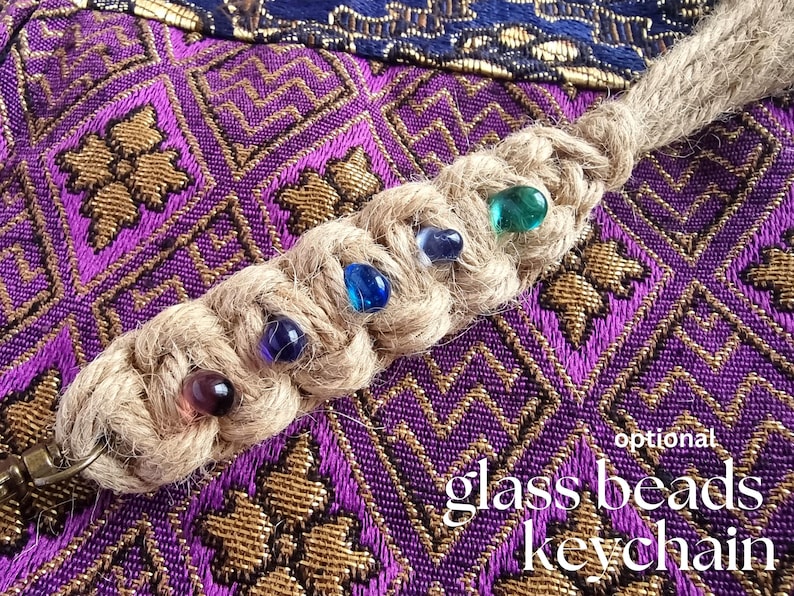 May include: A braided jute keychain with a metal ring and colorful glass beads. The keychain is on a purple and gold patterned fabric background. The text "glass beads keychain" is written in white on the fabric.