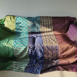 Könnte beinhalten: Eine mehrfarbige Patchwork-Decke mit geometrischem Muster. Die Decke ist aus einem weichen, luxuriösen Stoff gefertigt und in verschiedenen Farben gehalten, darunter Grün, Blau, Lila und Gold.