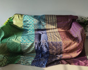 May include: A multi-colored patchwork throw blanket with a geometric pattern. The blanket is made of a soft, luxurious fabric and features a variety of colors, including green, blue, purple, and gold.