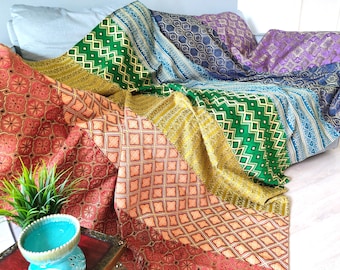 May include: A stack of colorful patterned throw blankets in shades of red, orange, yellow, green, blue, and purple. The blankets are folded and arranged on a couch.
