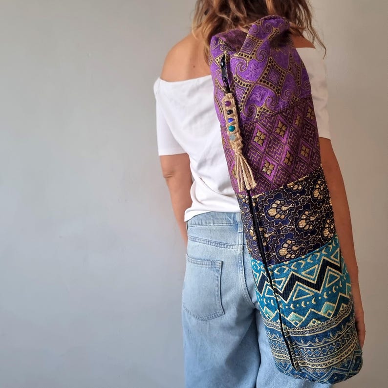 May include: A purple, blue, and gold yoga mat bag with a zipper closure and a tassel. The bag is made of patchwork fabric and has a beaded strap.