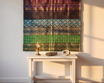 May include: A rectangular wall hanging featuring horizontal bands of intricate geometric patterns in shades of purple, blue, green, and gold. Below the textile, a white table holds a small brass oil lamp, a sage bundle, and a geode.